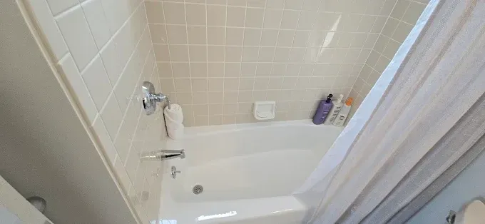 A white bathtub with a shower curtain and tiled walls.  Some toiletries are on the edge of the tub.
