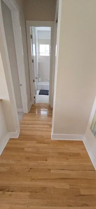 Wooden hallway leading to bathroom. White walls, bright wooden floors.
