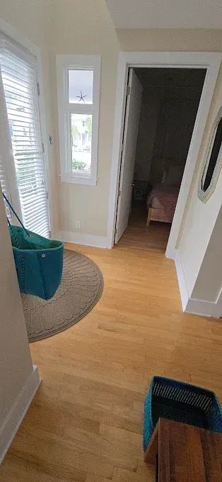 Hallway with wood floors, doorway to bedroom, blue bag hanging, round rug, small window.