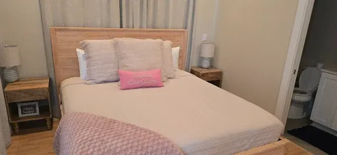Bedroom with bed, nightstands, and open bathroom door; pink pillow and blanket; neutral tones.