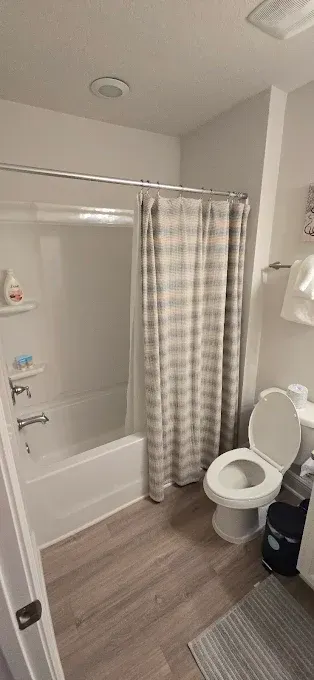 Bathroom with a shower, toilet, and striped shower curtain. The floor is wood-like.