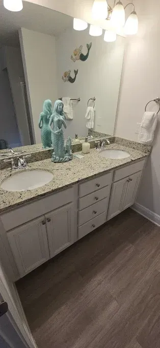 Bathroom with double sinks, white cabinets, mermaid decor, and wood-look flooring.