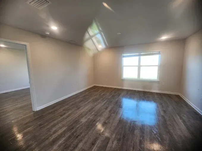 Empty room with wooden floor, window, and door. Beige walls, sunlight.