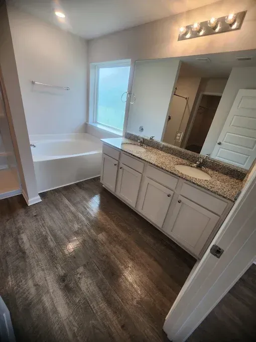 Bathroom with white vanity, granite countertop, and wood-look floor; bathtub and window visible.