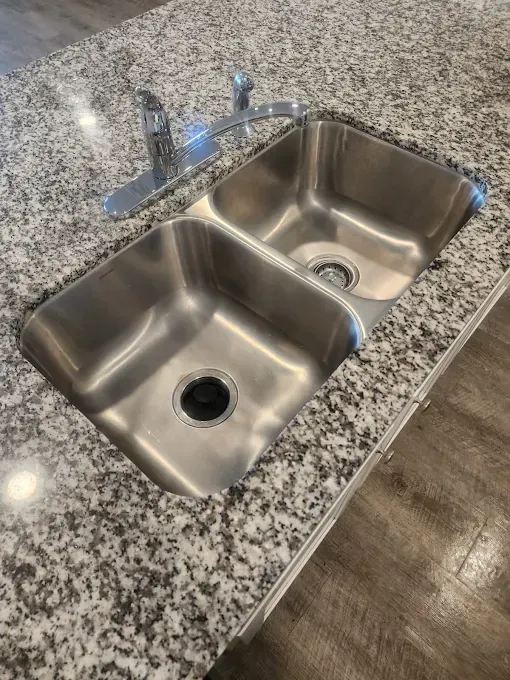 Double stainless steel kitchen sink with faucet on granite countertop.