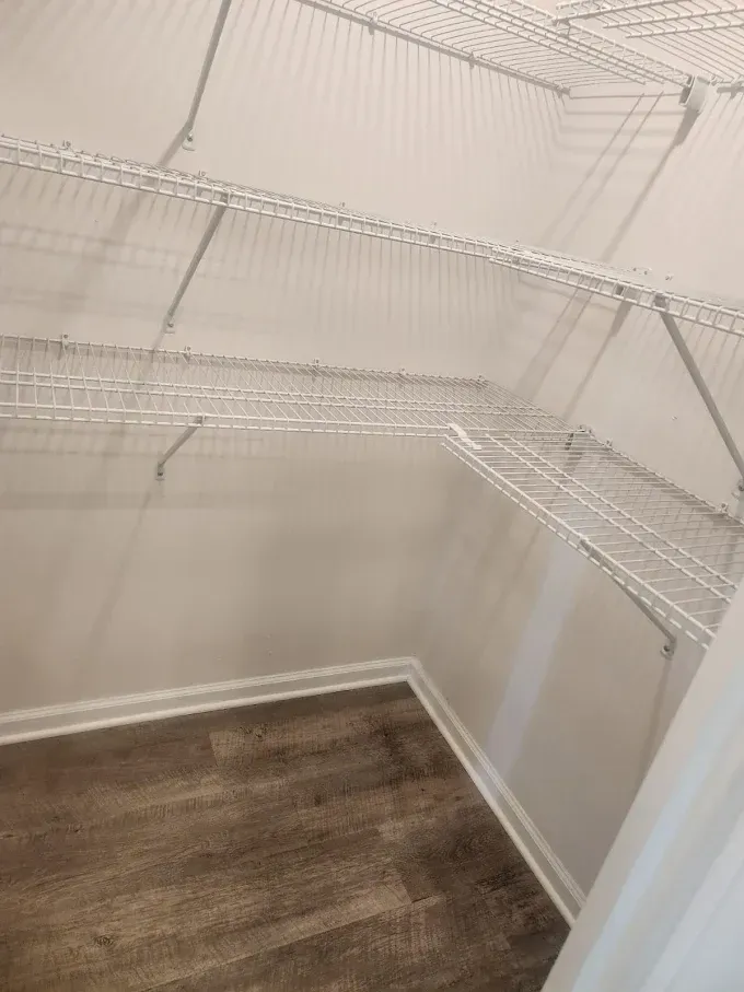 Empty closet with wire shelves on white walls; wood-look flooring.