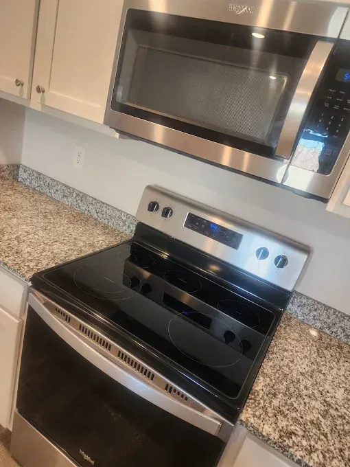 Stainless steel oven and microwave in a kitchen with granite countertops and white cabinets.