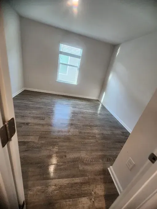 Empty room with angled walls, wood-look flooring, and a window with blinds.