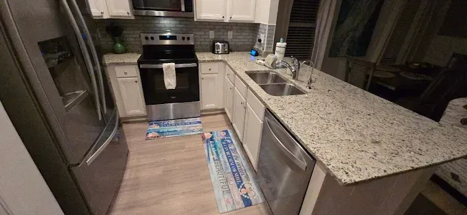 Kitchen with white cabinets, stainless steel appliances, granite countertops, and coastal-themed rugs.
