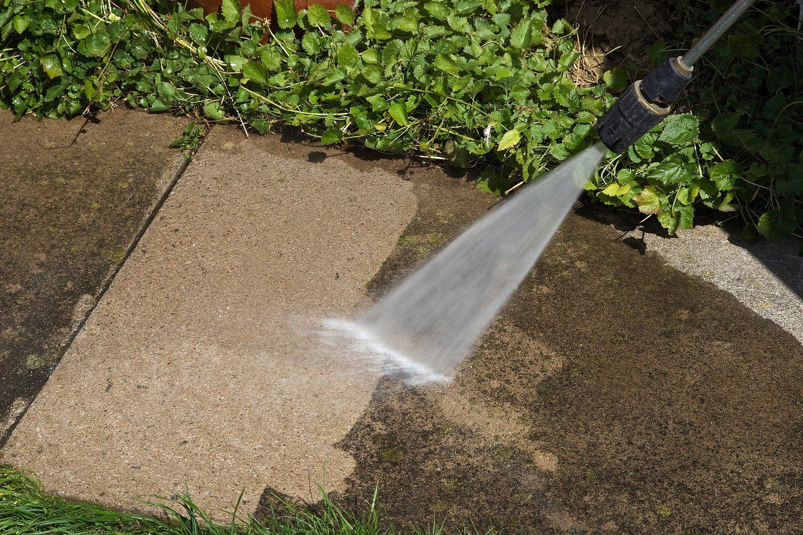 Pressure washing a concrete surface, removing dirt.
