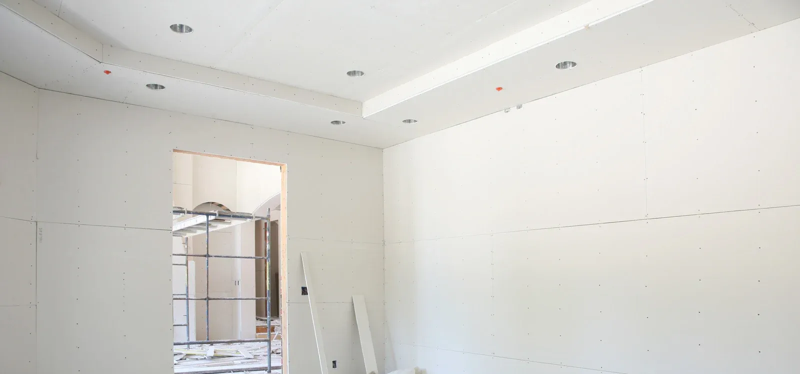 A white room under construction; a doorway in the middle; a drop ceiling with recessed lighting.