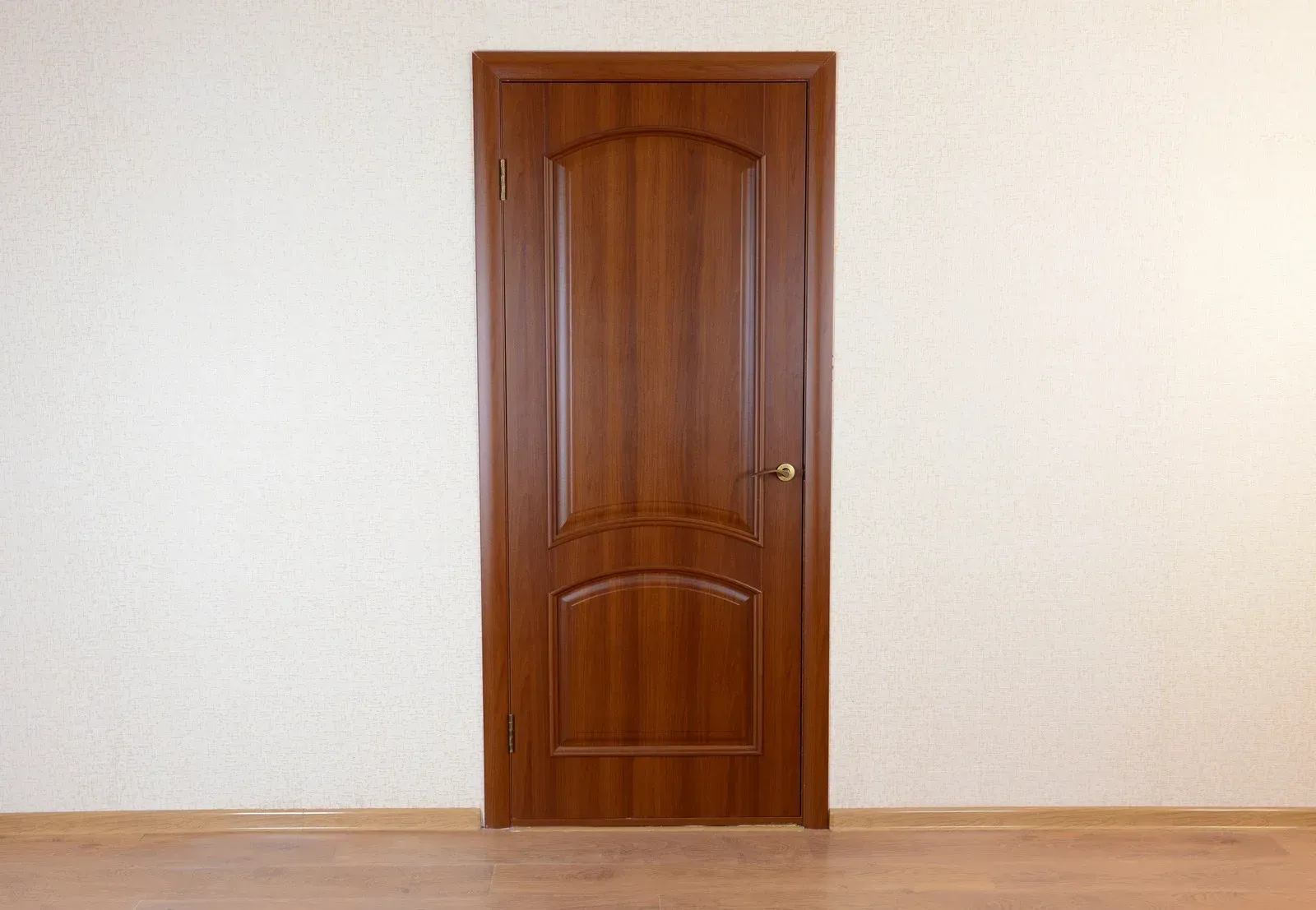 Brown wooden door in a white room with a light brown floor.