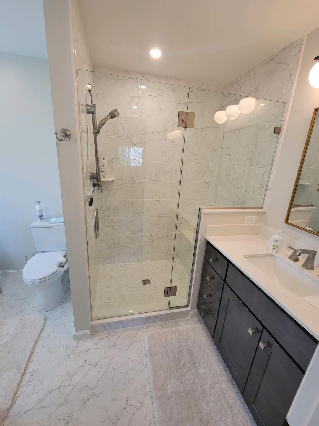 Modern bathroom with a glass shower, vanity, and white marble tile flooring.