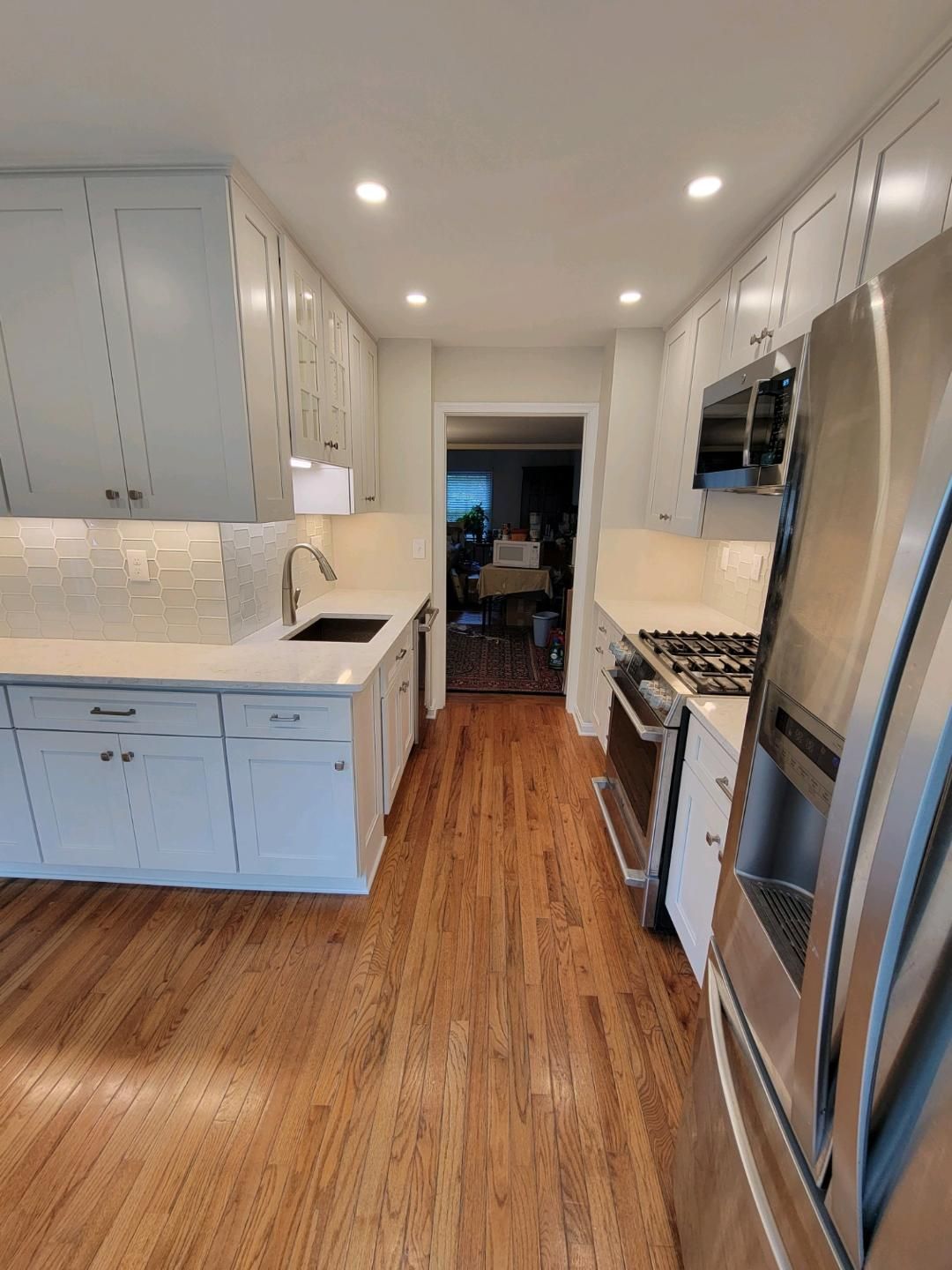 Narrow, galley kitchen with white cabinets, stainless steel appliances, and wood floors.