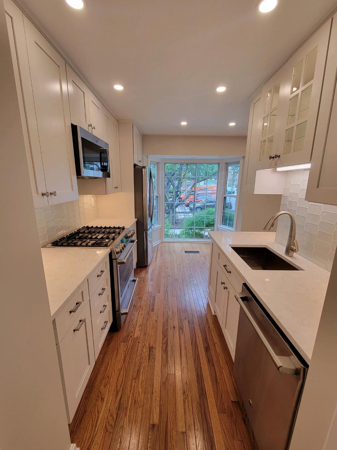 Narrow kitchen with white cabinets, stainless steel appliances, and wood floors.