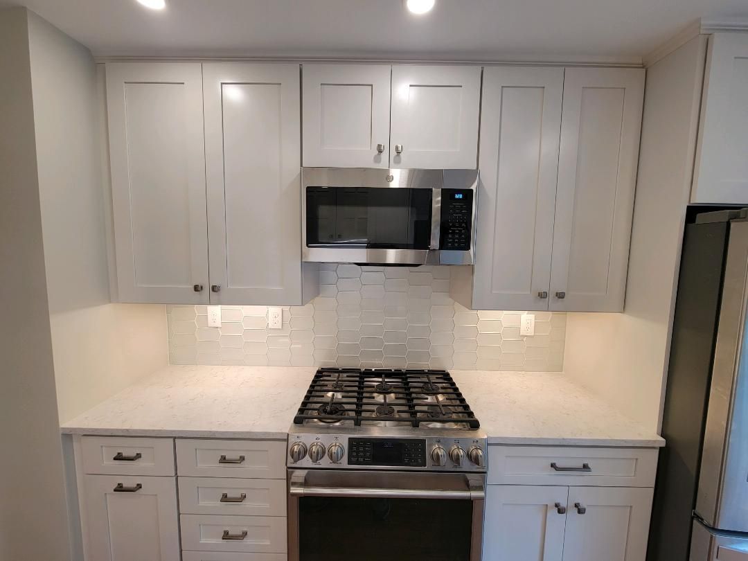 White kitchen with cabinets, stainless steel oven, microwave, and backsplash.