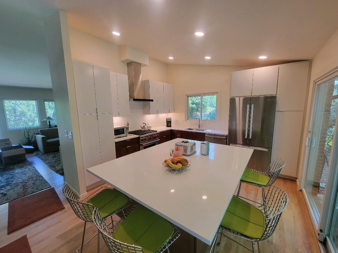 Modern kitchen with a large island, white cabinets, stainless steel appliances, and green bar stools.