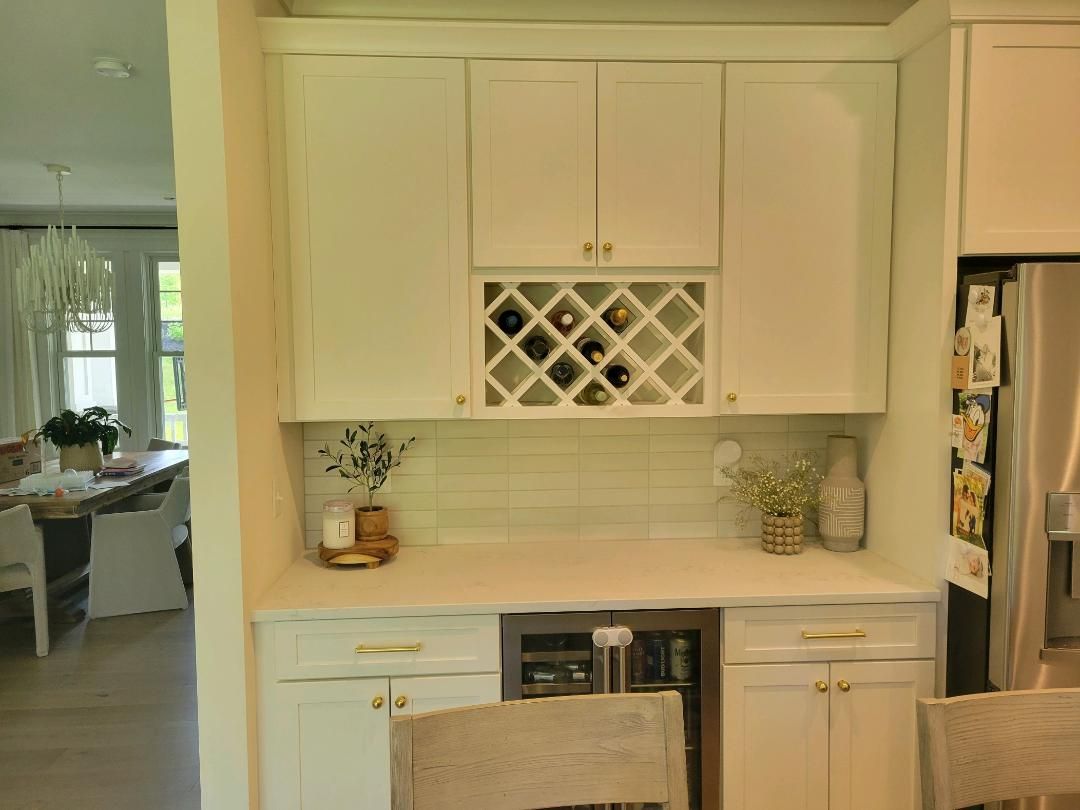 White built-in kitchen bar with wine rack, cabinets, counter, and wine cooler. Adjacent to dining area.