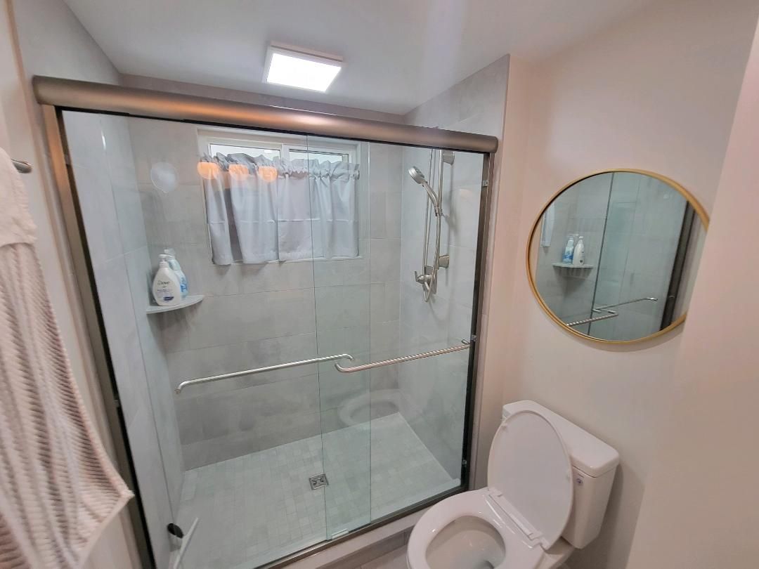 Bathroom with a glass shower, toilet, and round mirror.
