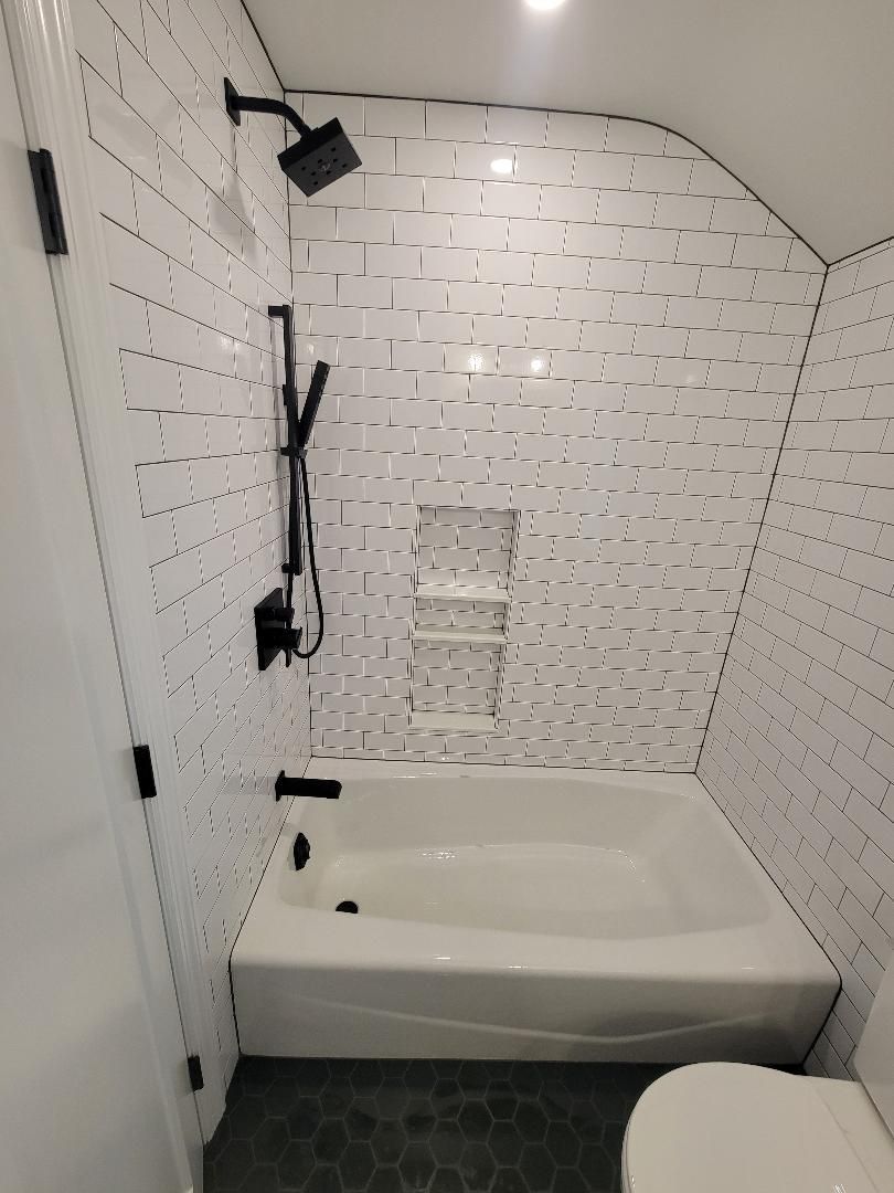 A modern bathroom with a white bathtub, black shower fixtures, and patterned white tile walls.