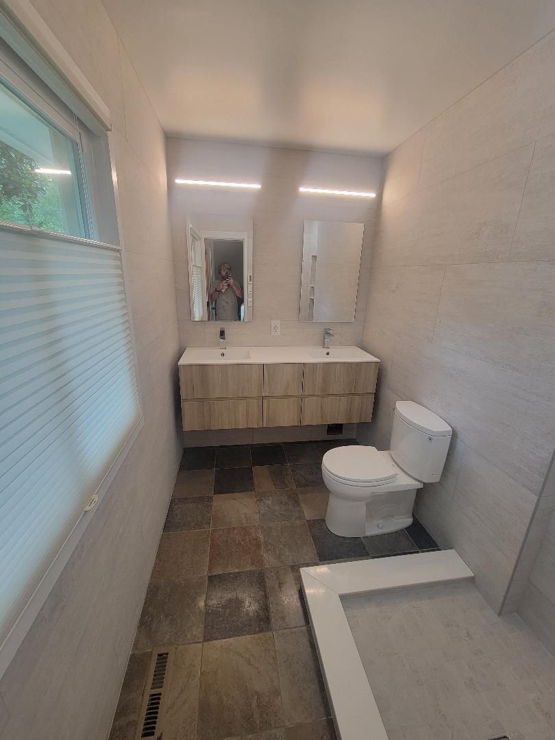 Modern bathroom with a wood vanity, two mirrors, and a toilet; neutral colors.
