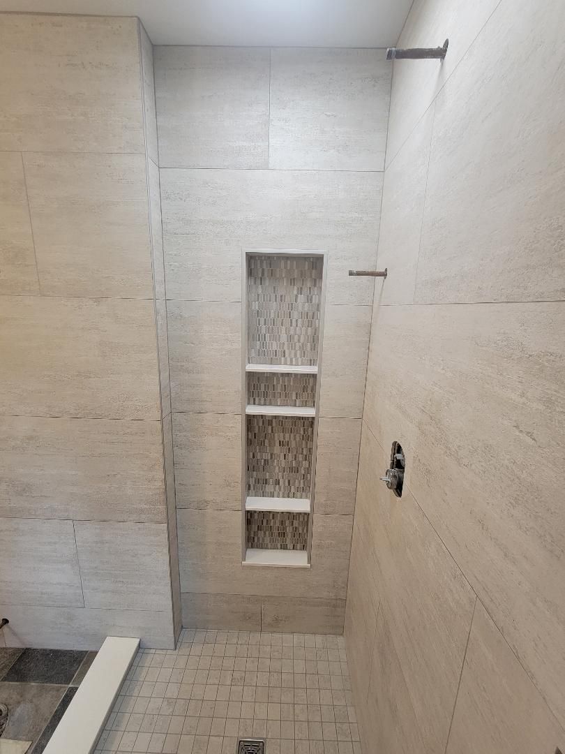 Bathroom shower with light stone tile, niche with shelves, and showerhead.