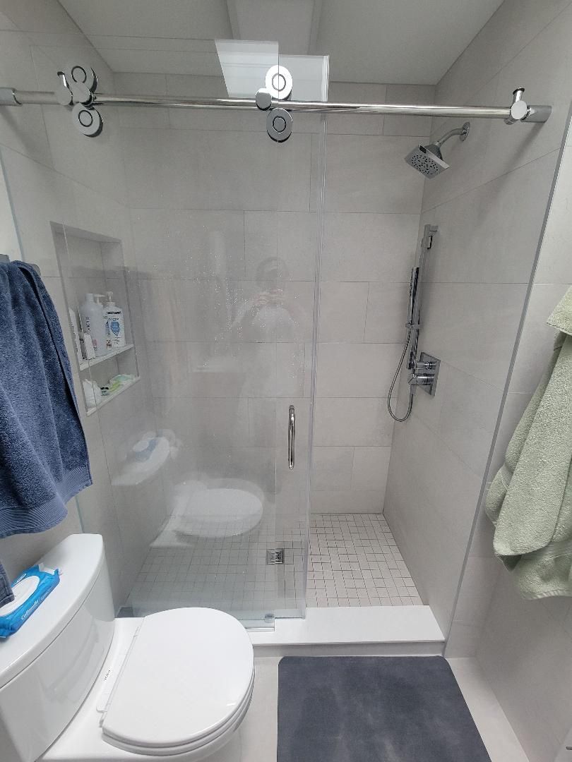 A small, modern bathroom with a glass shower, toilet, and blue and green towels.