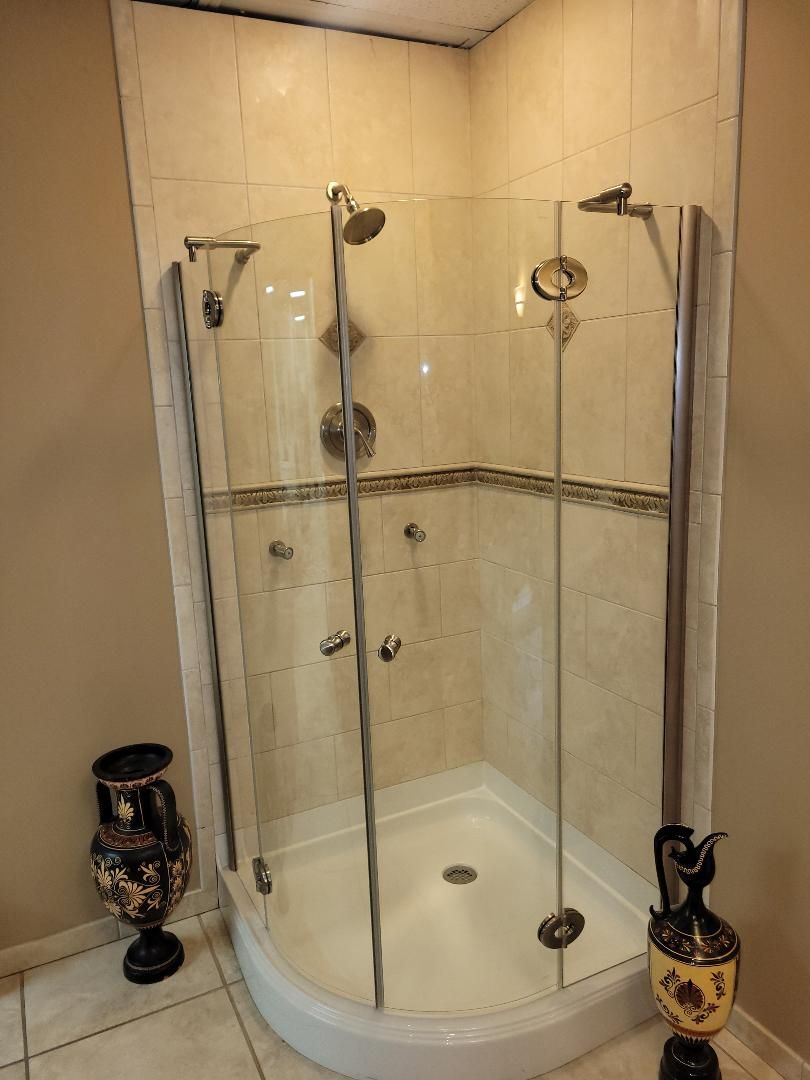 A clear glass shower enclosure with multiple showerheads and body jets, set in a beige tiled bathroom.