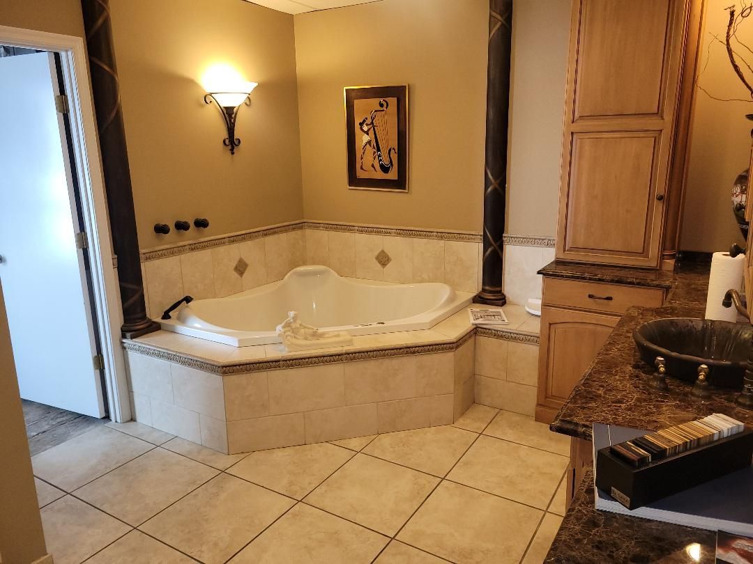 Bathroom with a built-in corner bathtub, tan walls, light tile floor, and wooden cabinets.