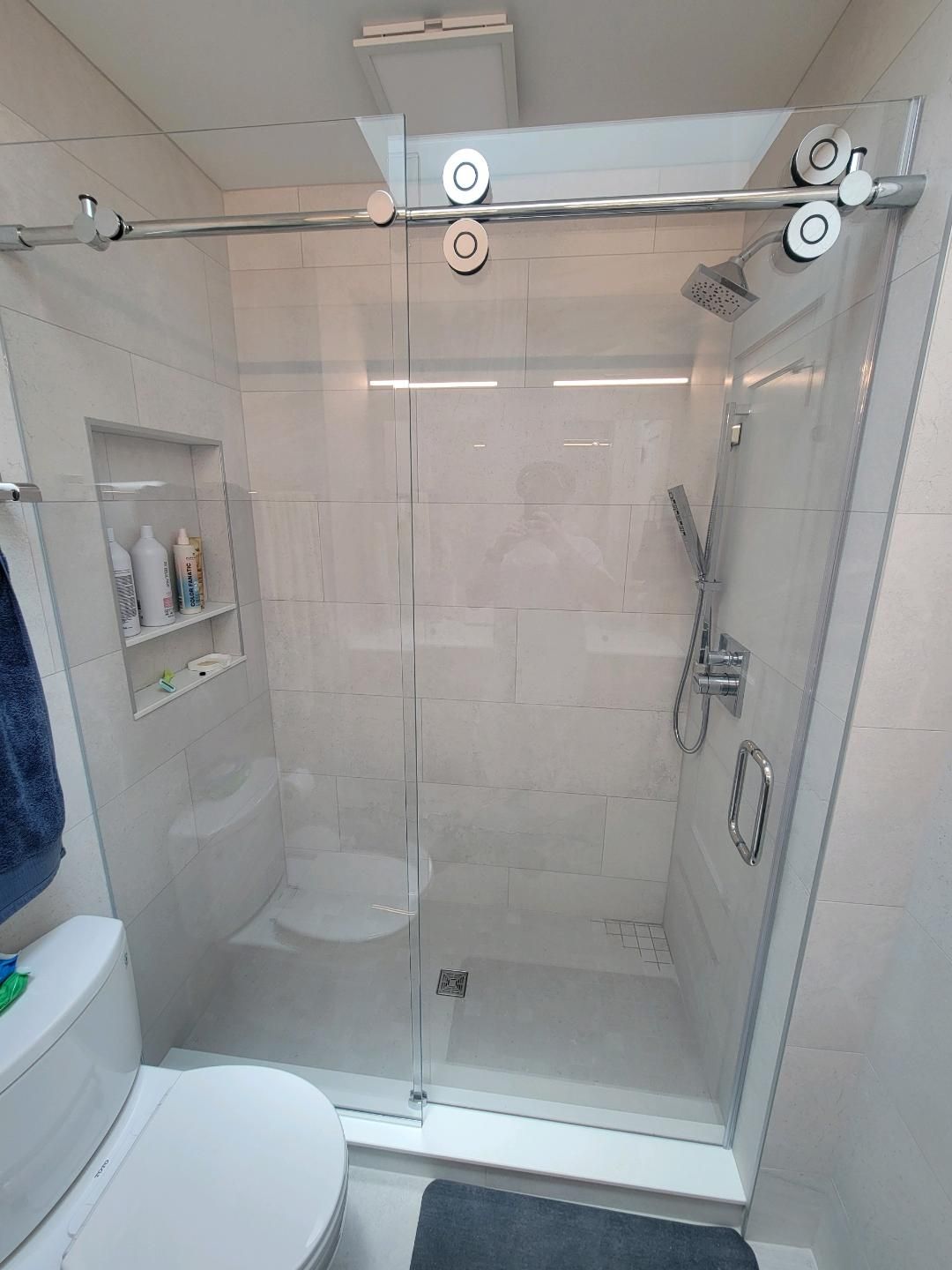 Modern bathroom with a glass shower, white tile, and chrome fixtures.