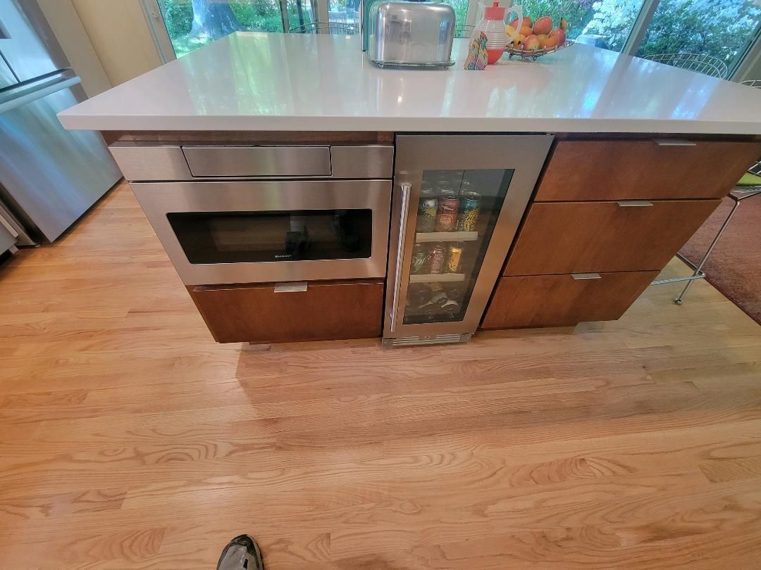 Kitchen island with microwave, beverage cooler, drawers, and wooden floor.