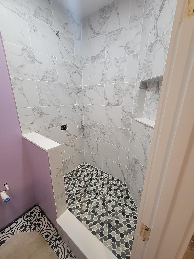 Bathroom with marble-look shower tiles, mosaic floor, built-in shelf, and a partly visible lavender wall.