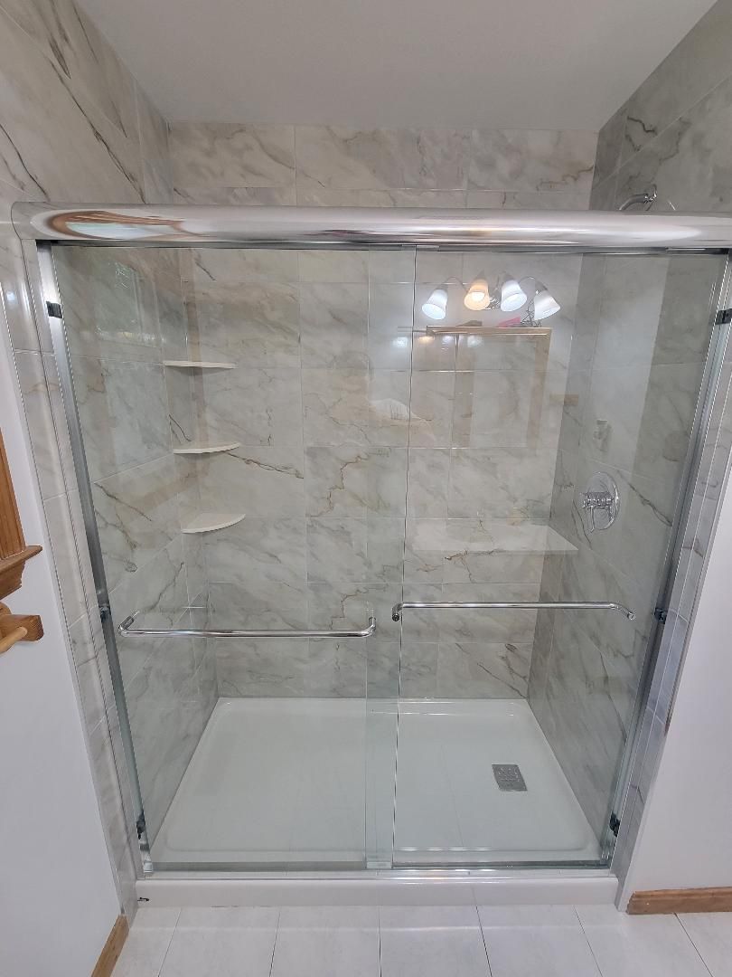 Shower with sliding glass doors, white base, beige and grey marbled wall, chrome hardware.