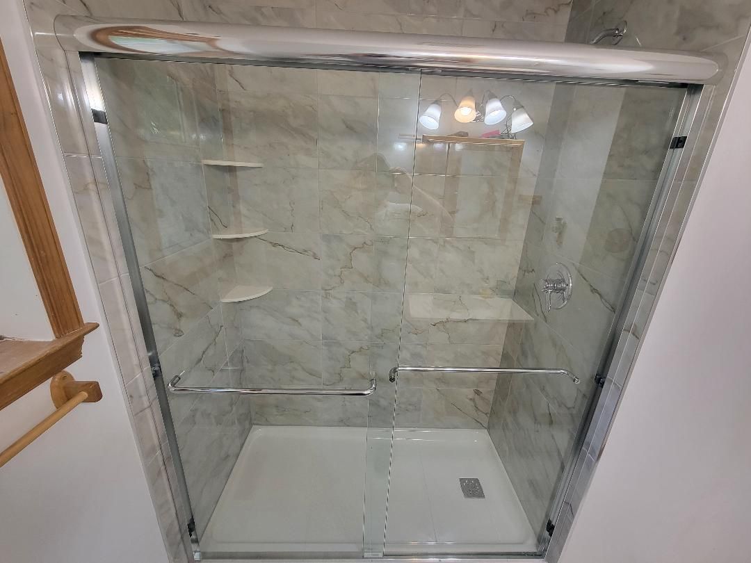 Shower with sliding glass doors and light-colored marble-like tile.