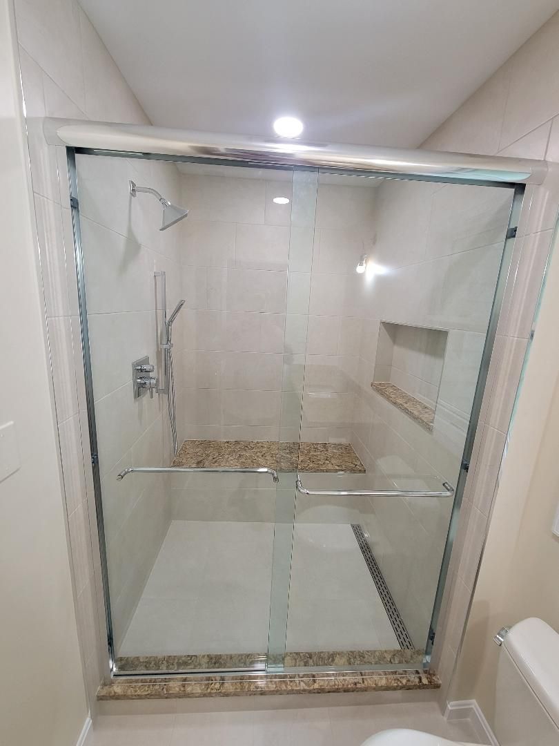 Modern shower with glass doors, beige walls, and stone bench.