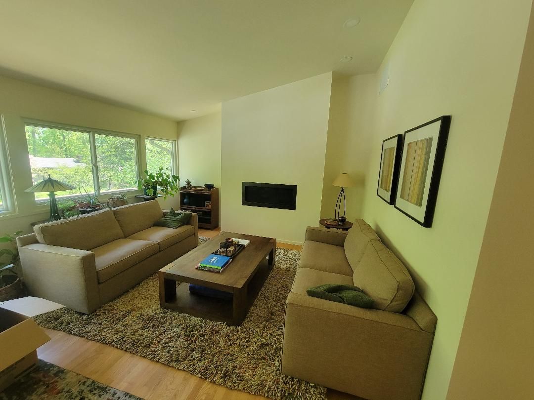 Living room with two beige sofas, a rug, and a coffee table. A fireplace and large window are visible.