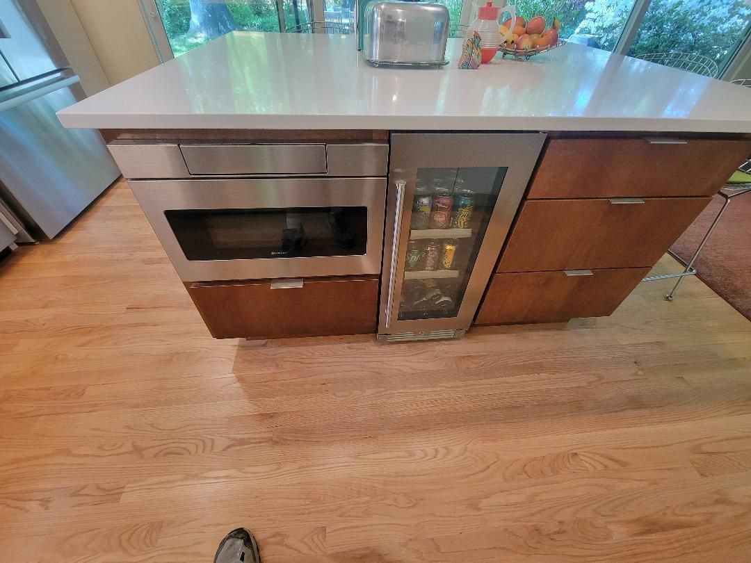 Kitchen island with built-in microwave, beverage fridge, and drawers; hardwood floors.