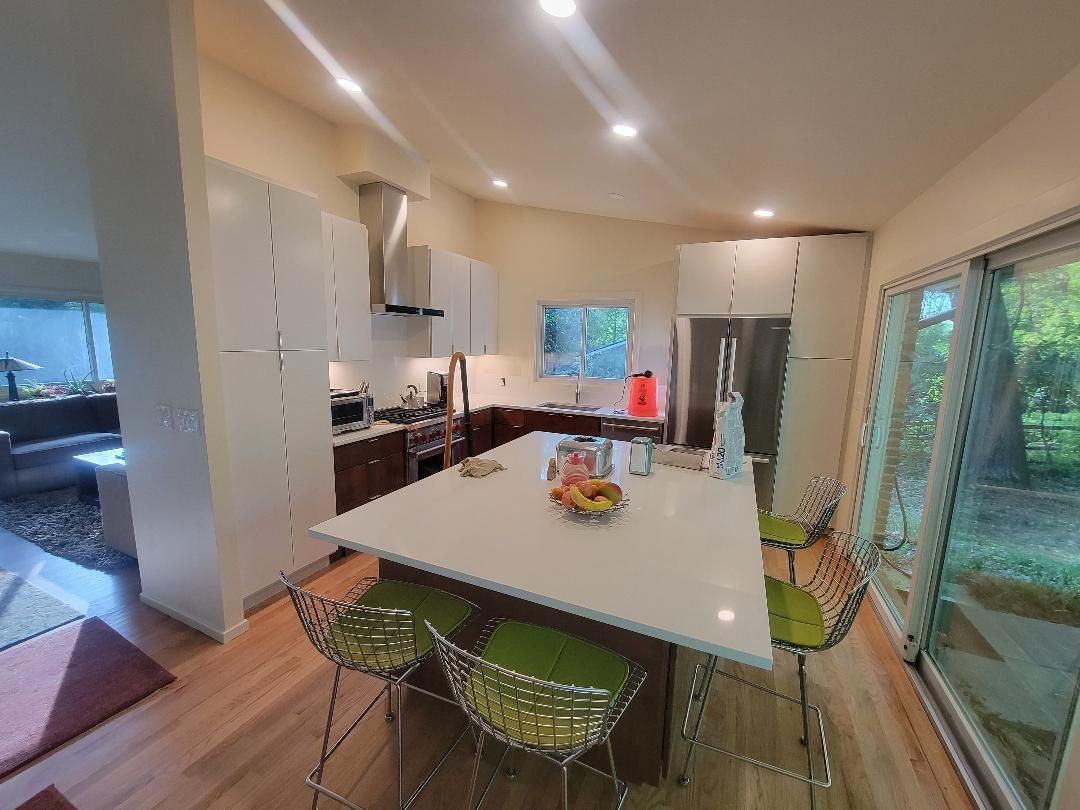 Modern kitchen with white cabinets, island, and stainless steel appliances. Green barstools, window with outdoor view.