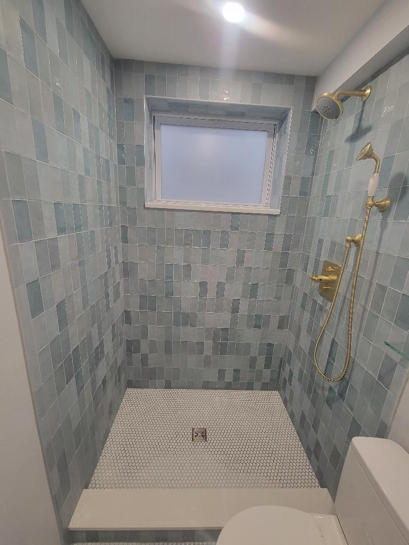 Small shower with blue tile, gold fixtures, and a window.