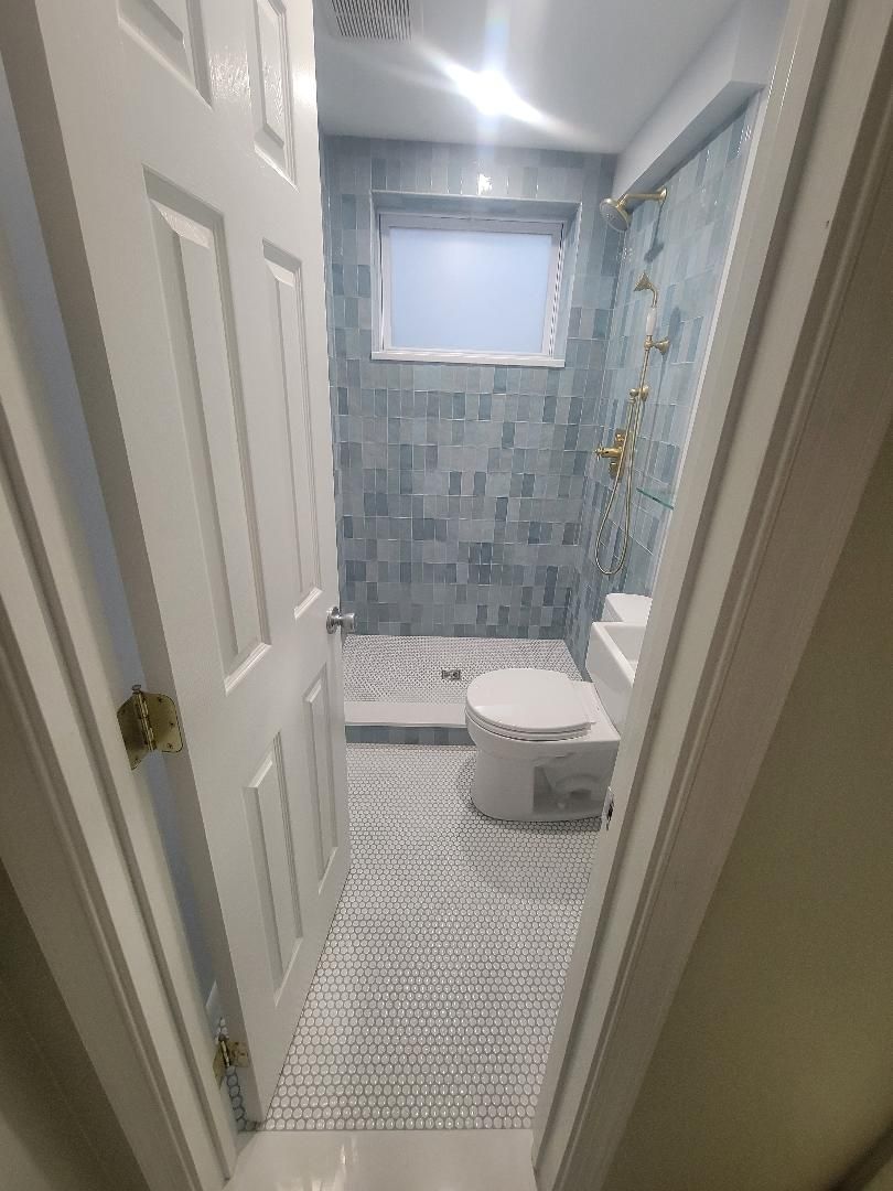 Bathroom with blue tile shower, white toilet, patterned floor, viewed from doorway.