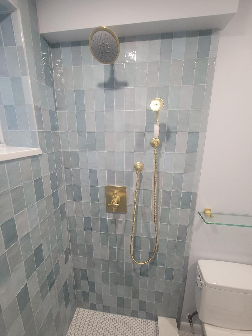 Blue tiled shower with gold fixtures, including a shower head, handheld sprayer, and faucet.