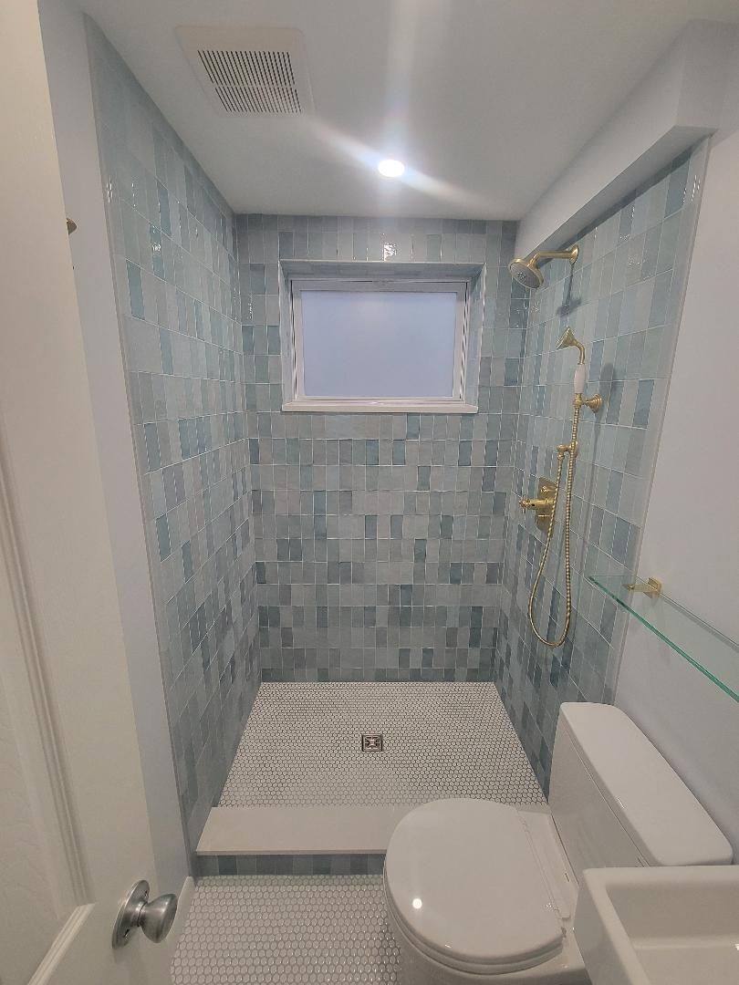 Small bathroom with blue tile shower and gold fixtures; toilet and sink.