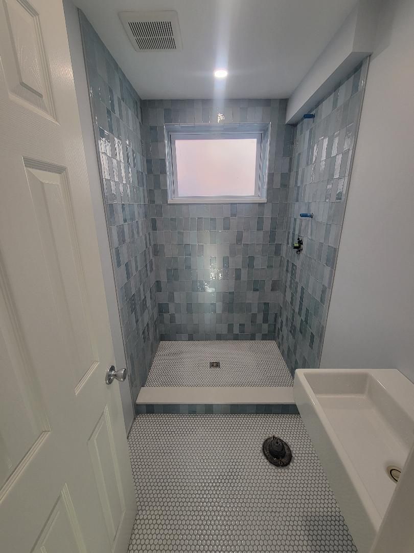 Small bathroom with blue tile shower, white sink, and patterned floor.