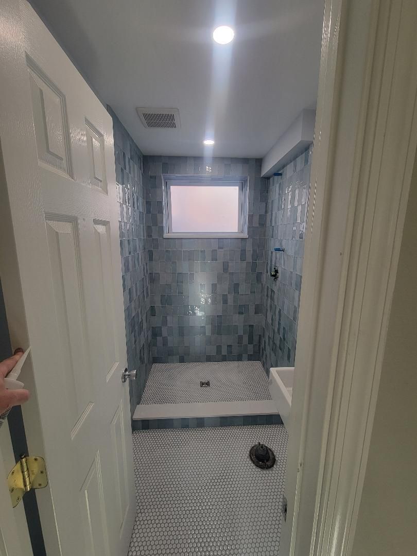 Newly renovated bathroom with blue tiled shower, penny tile floor, and open door.