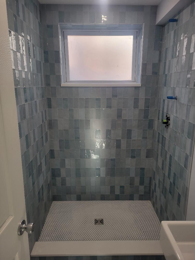 Blue-tiled shower with window and patterned floor; white door visible on the left.