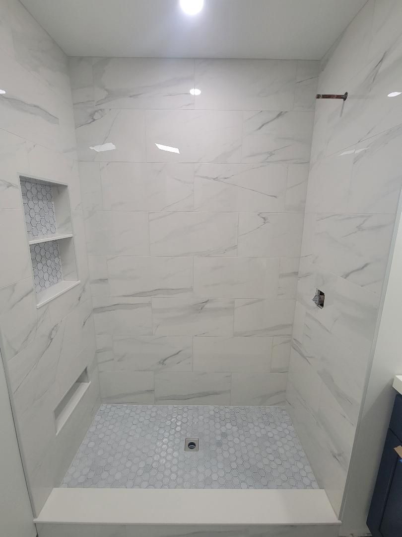 White tiled shower with a pebble stone floor, built-in shelves, and silver fixtures.