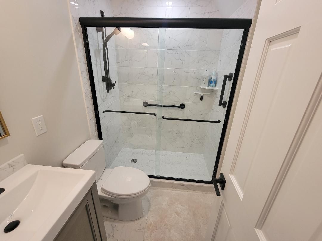 Bathroom with white tiles, glass shower, black fixtures, and toilet.