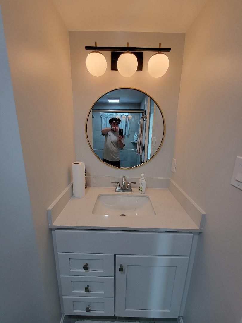 Bathroom vanity with a round mirror, white cabinet, sink, and a three-bulb light fixture.