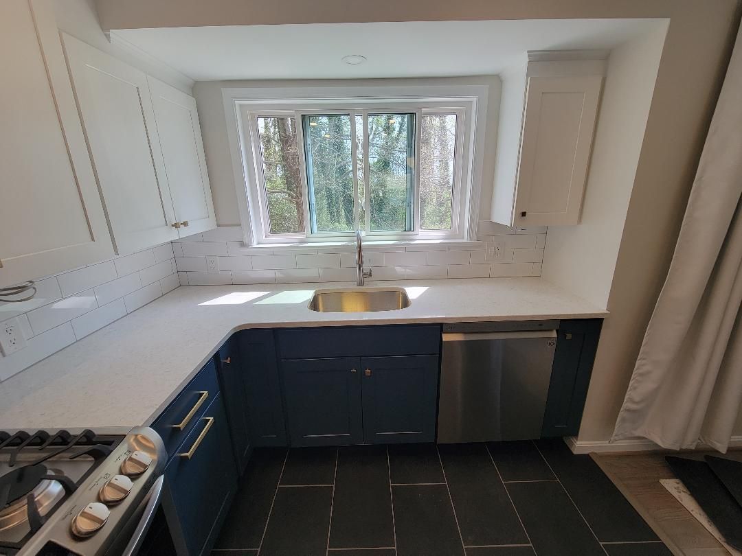 Kitchen with blue cabinets, white countertops, stainless steel appliances, and a window overlooking trees.