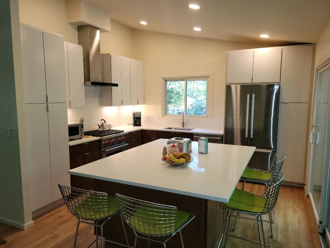 Modern kitchen with white cabinets, dark wood accents, island with seating, stainless steel appliances.